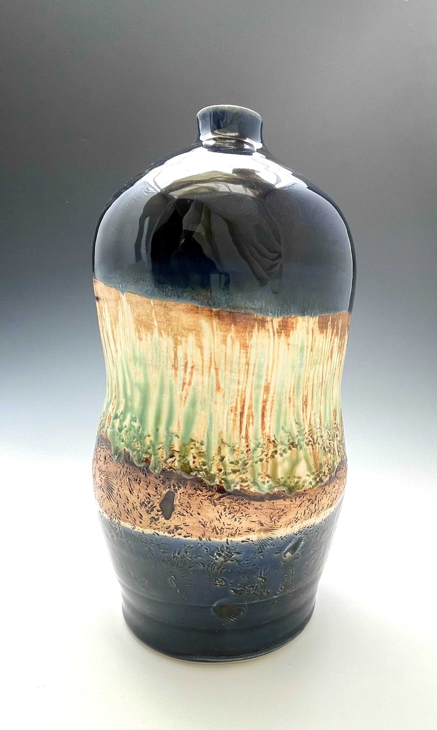 tall porcelain wheel-thrown sculptural vase with dark blue, brown and light green glazes representing a river's edge