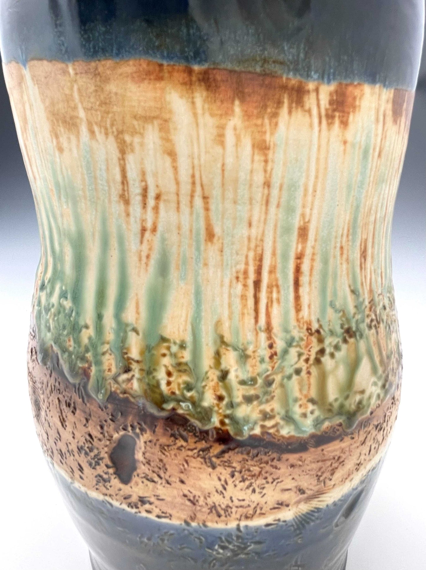 detail of surface of tall porcelain wheel-thrown sculptural vase with dark blue, brown and light green glazes representing river grasses