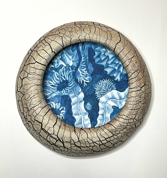wall-hung sculpture with a blue and white painting of tide pool imagery and creatures, within a cracked texture, round tan-color ceramic form