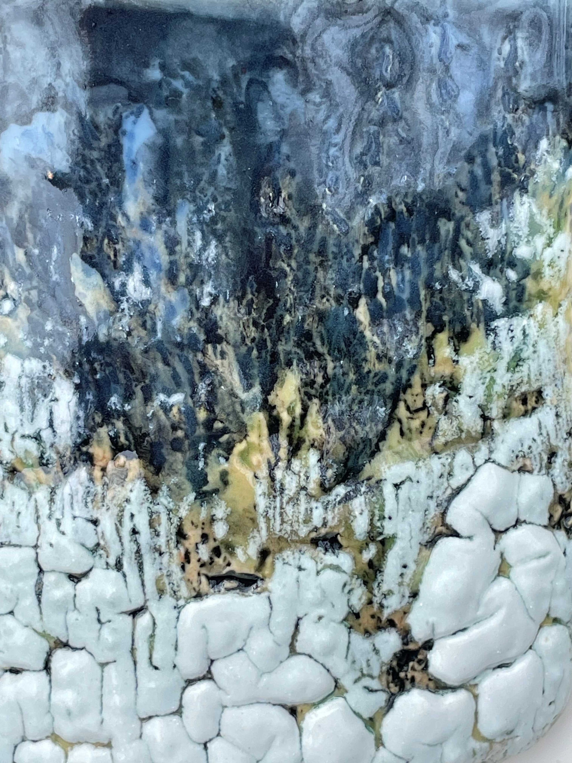 detail of glazed surface with layered white, blue, dark grey and light green colored glazes on a textured surface