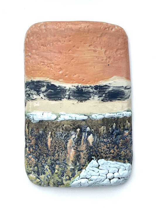 Rectangular porcelain wall-hung sculptural tile with coral, white, grey and green glazes on a textured surface, representing an abstract sunset landscape scene
