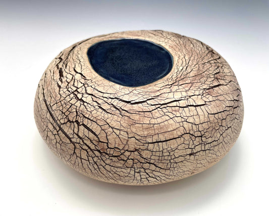 A stone-shaped ceramic sculpture with an earth-toned crackle surface and a pool of dark blue glaze
