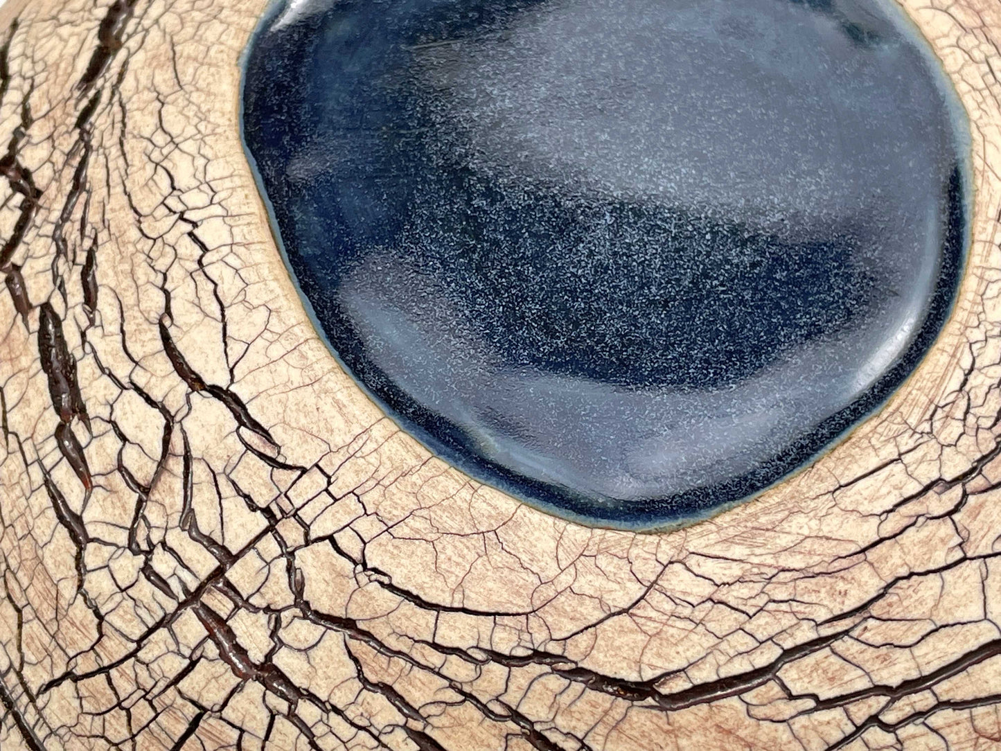 detail, close-up  of a ceramic sculpture with an earth-toned crackle textured surface and a pool of dark blue glaze