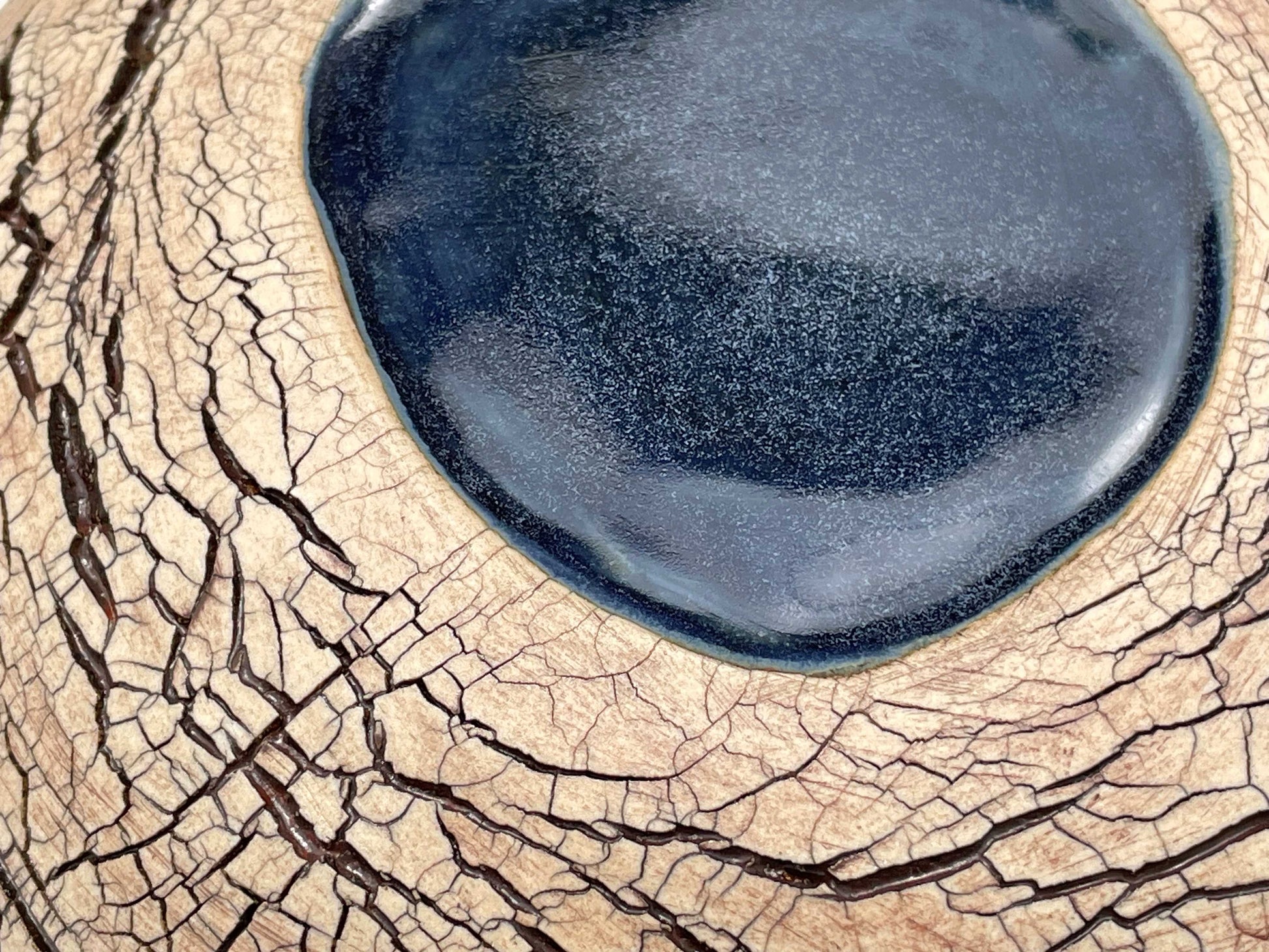 detail, close-up  of a ceramic sculpture with an earth-toned crackle textured surface and a pool of dark blue glaze