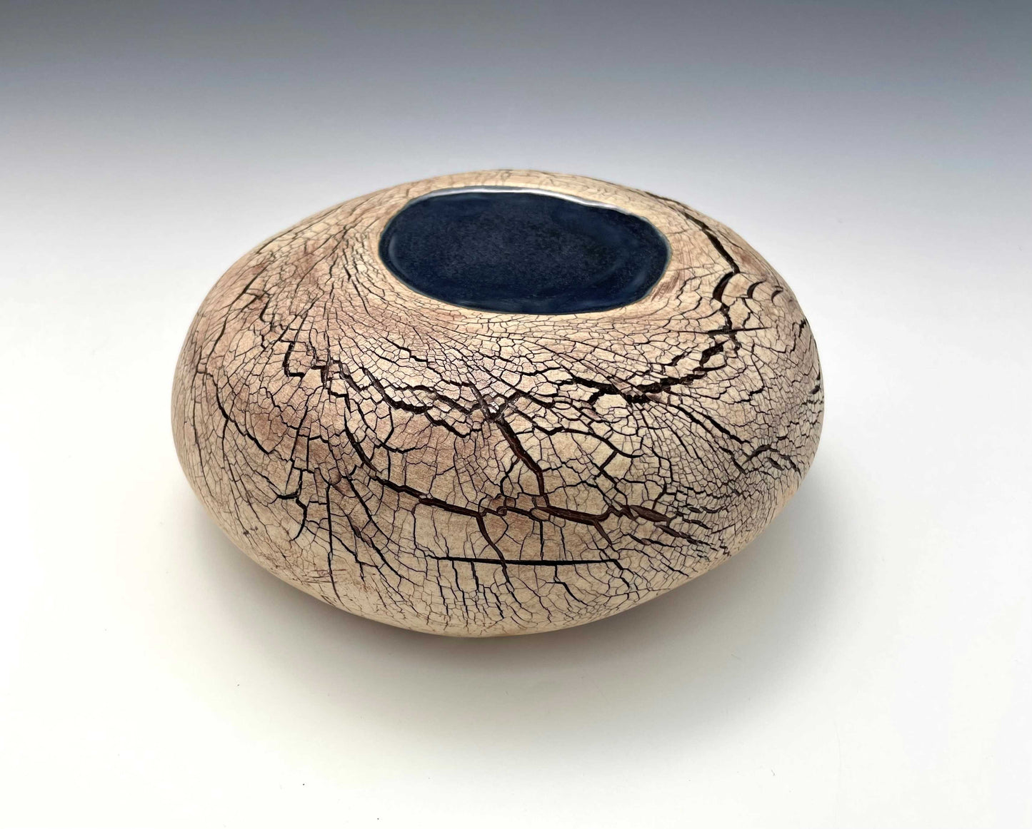 A stone-shaped ceramic sculpture with an earth-toned crackle surface and a pool of dark blue glaze