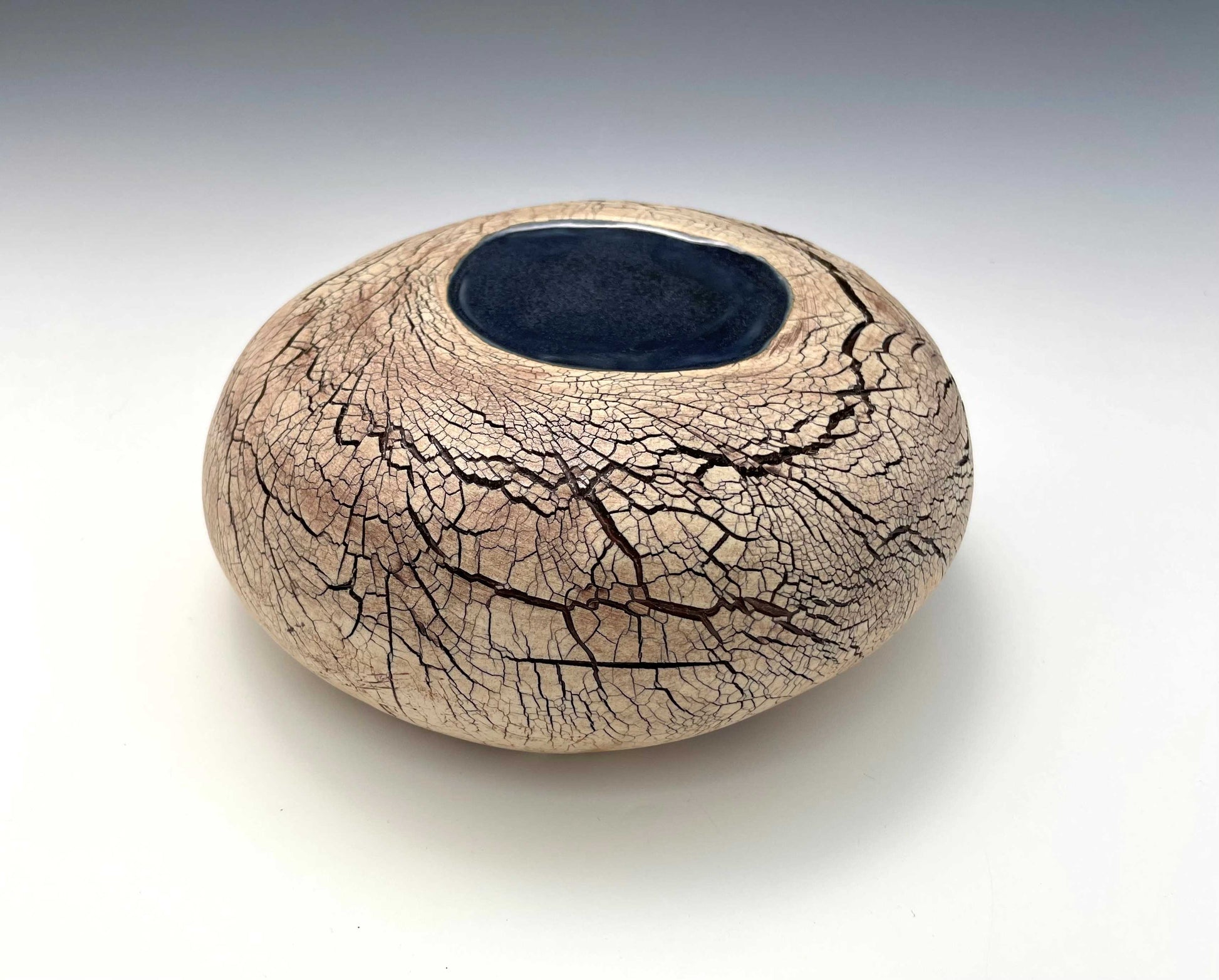 A stone-shaped ceramic sculpture with an earth-toned crackle surface and a pool of dark blue glaze