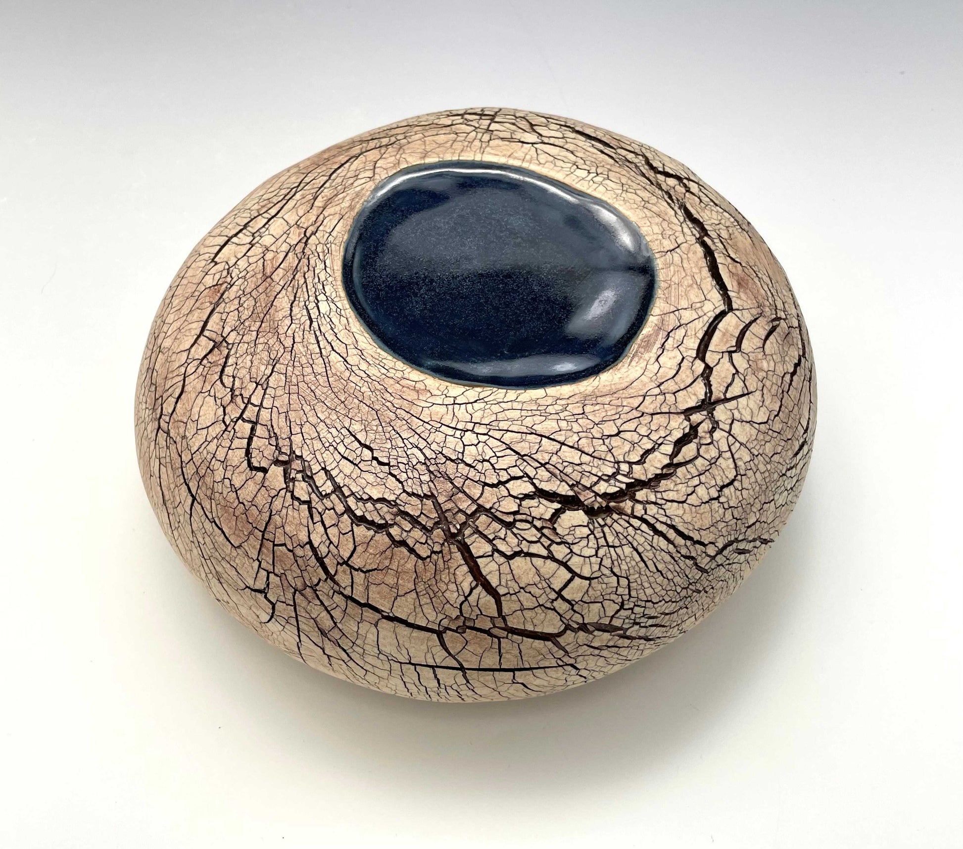 overhead view of a stone-shaped ceramic sculpture with an earth-toned crackle surface and a pool of dark blue glaze