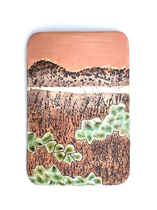 Rectangular porcelain wall-hung sculptural tile with coral, brown and green glazes on a textured surface, representing an abstract sunset landscape scene