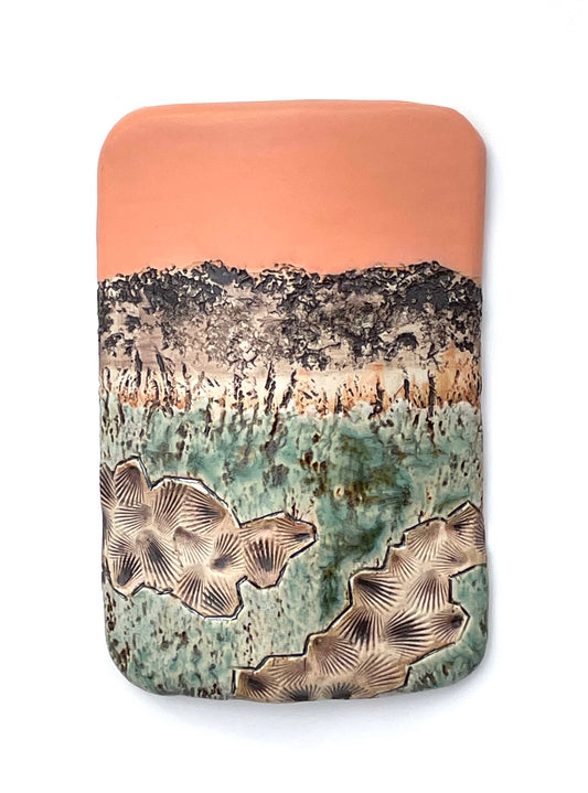 Rectangular porcelain wall-hung sculptural tile with coral, white, brown and green glazes on a textured surface, representing an abstract sunset landscape scene
