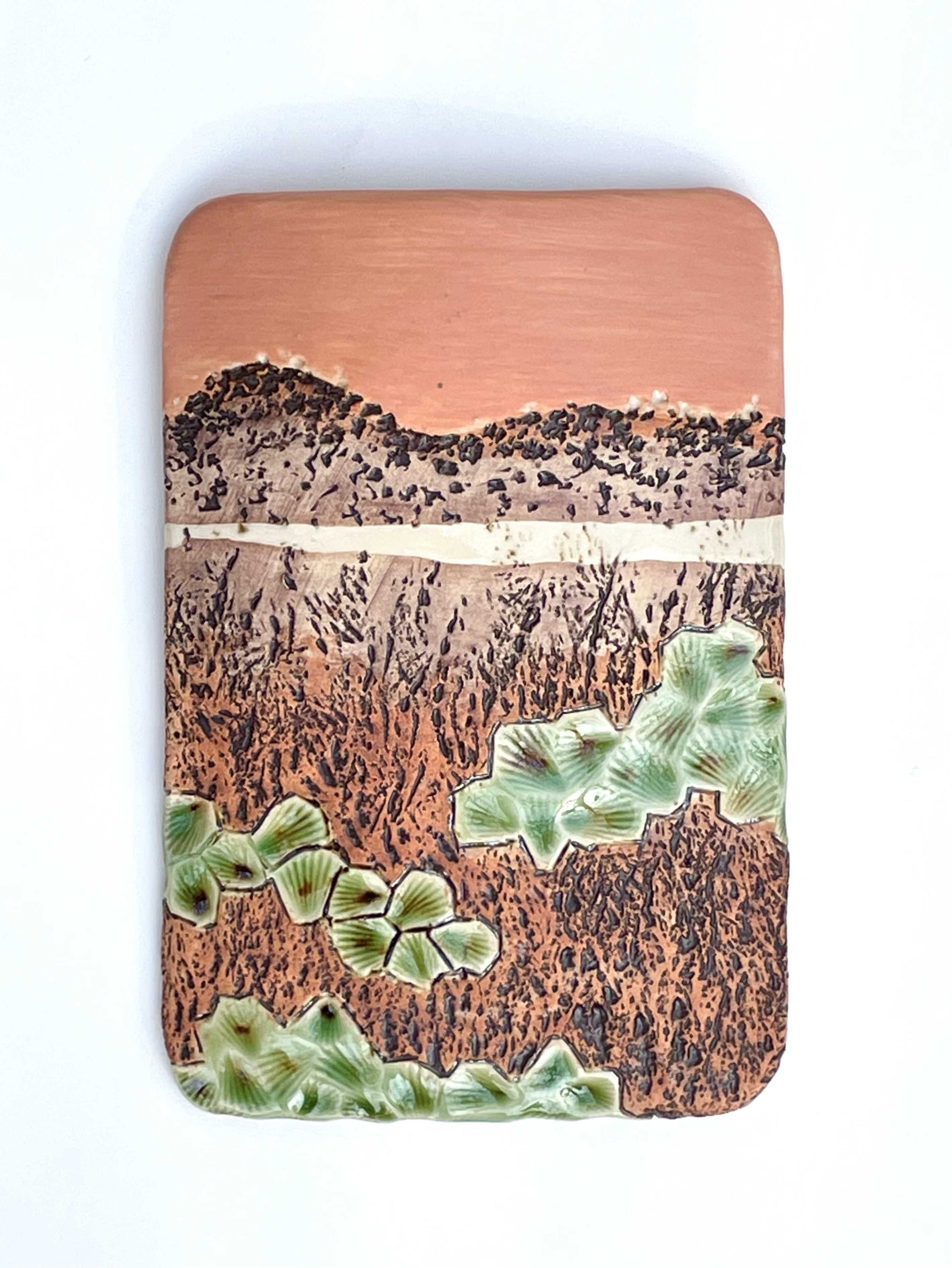 Rectangular porcelain wall-hung sculptural tile with coral, brown and green glazes on a textured surface, representing an abstract sunset landscape scene