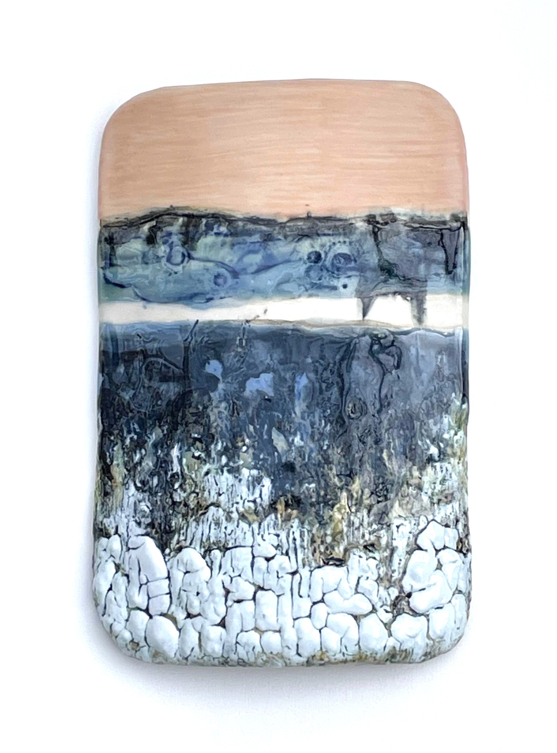 Rectangular porcelain wall-hung sculptural tile with coral, white, blue and dark grey glazes on a textured surface, representing an abstract sunset landscape scene