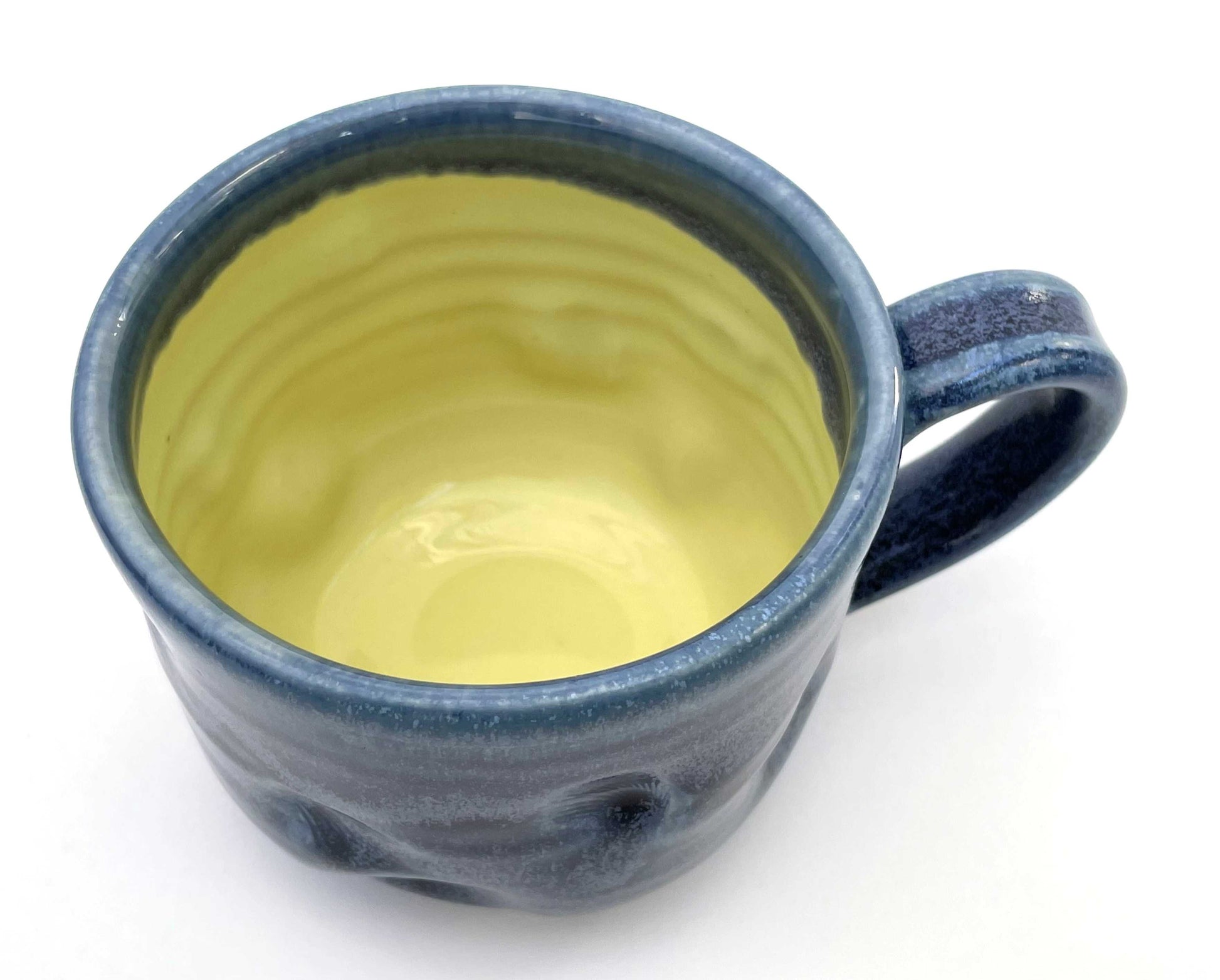 Blue ceramic mug with a textured surface and a yellow glazed interior