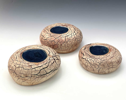 A group of three stone-shaped ceramic sculptures with a crackle surface and pools of dark blue glaze